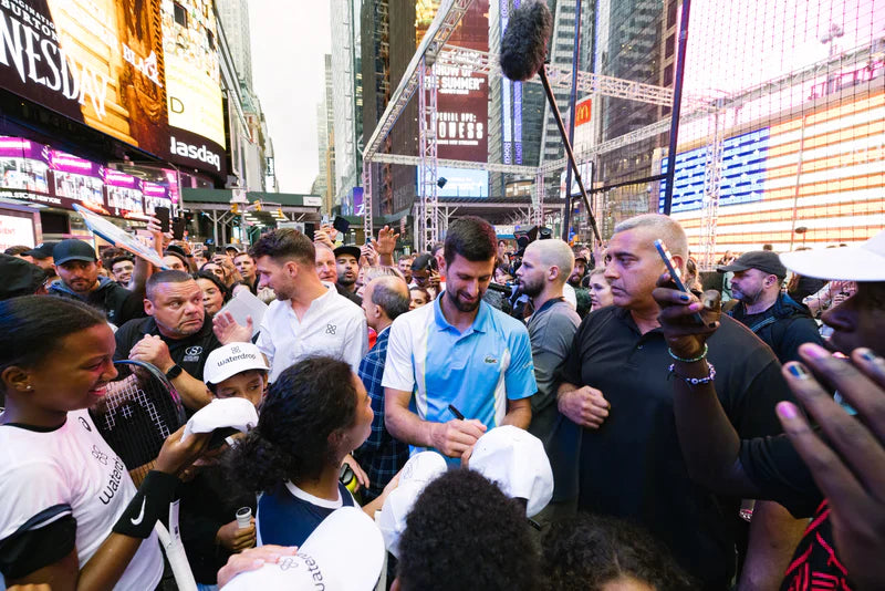 A group of people in a city, including a man in a blue shirt and a woman holding a tennis racket.