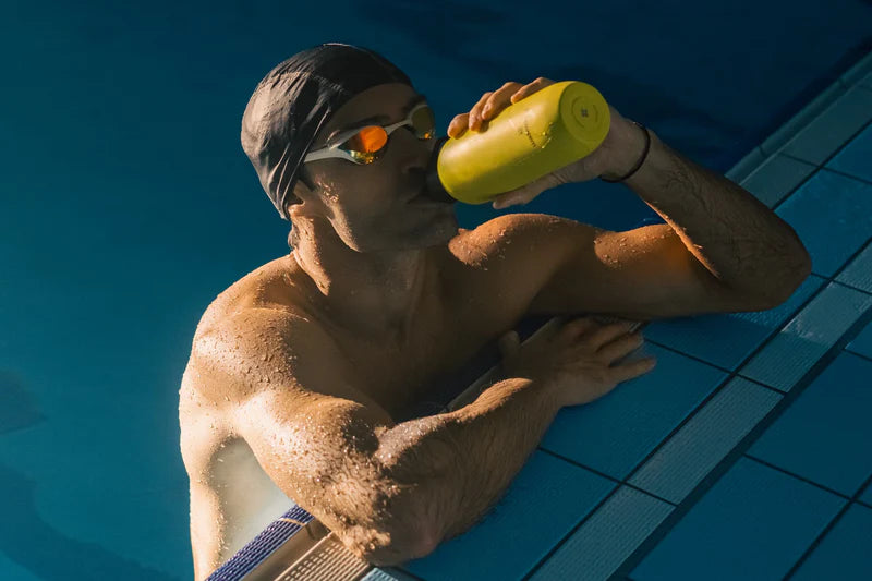 A man in a swimming pool drinks from a yellow waterdrop® bottle, highlighting hydration solutions.