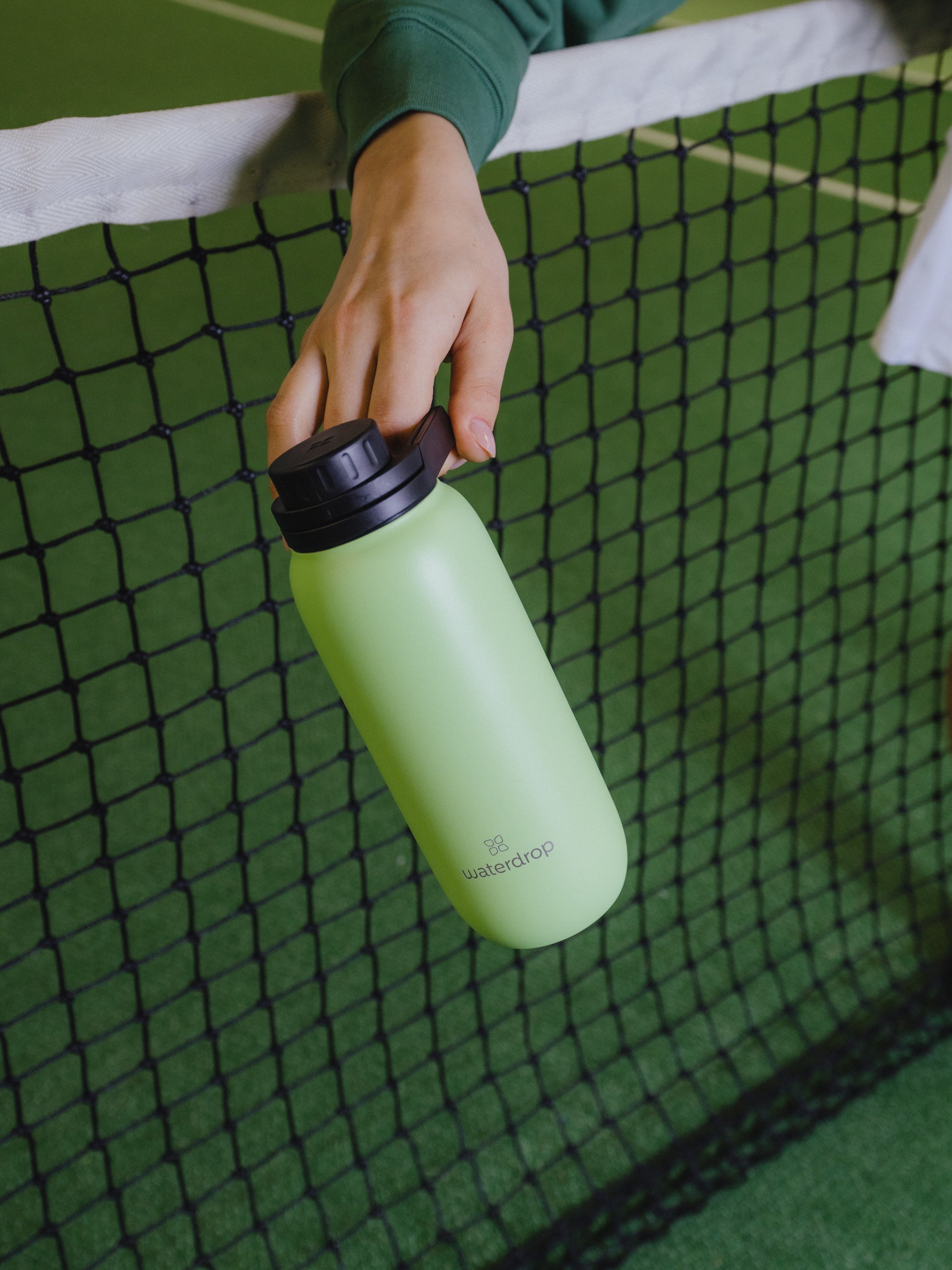 A hand holding a green waterdrop® branded water bottle with a black lid.