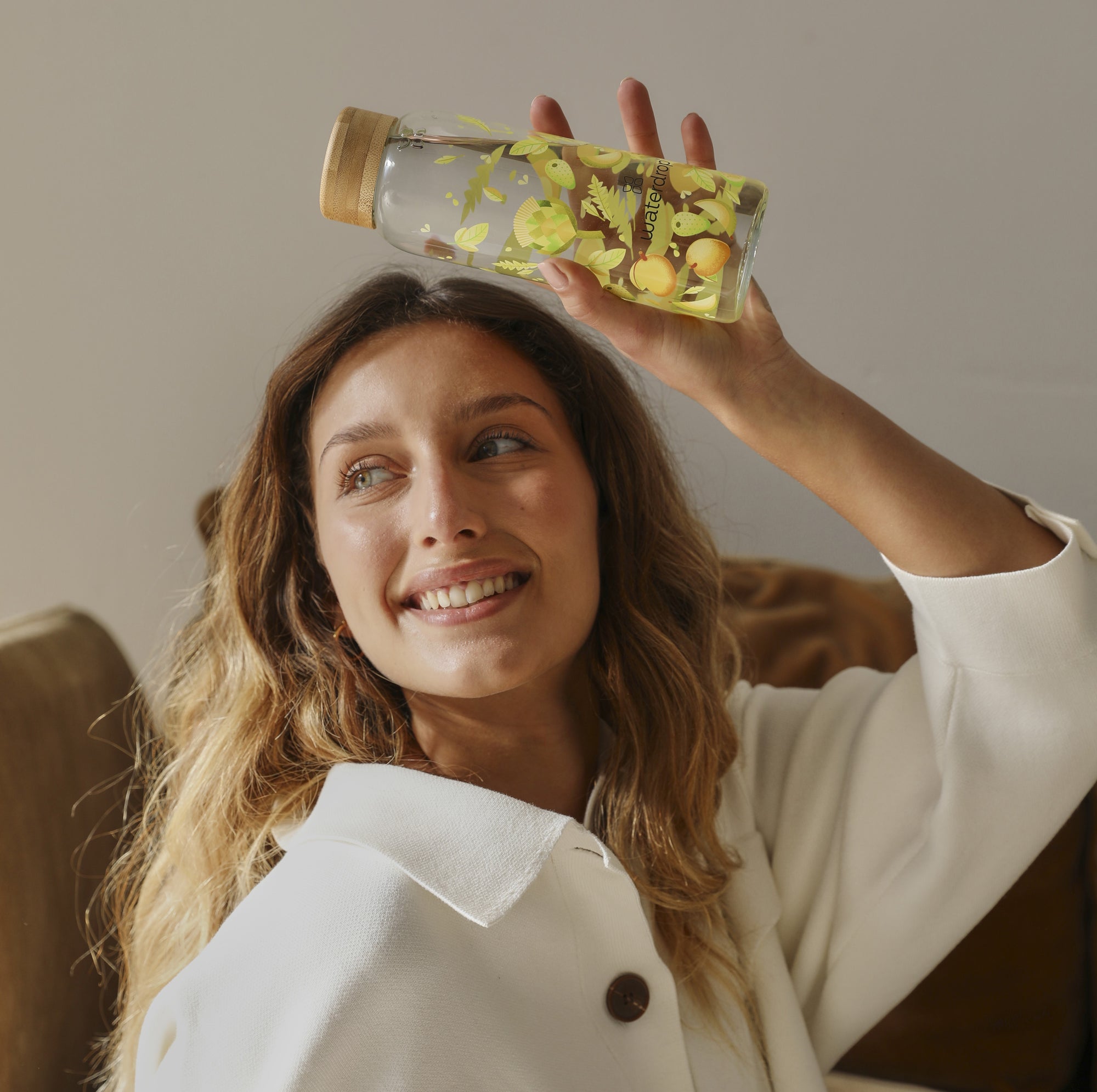 A woman with long hair holding a waterdrop® branded glass water bottle, smiling.