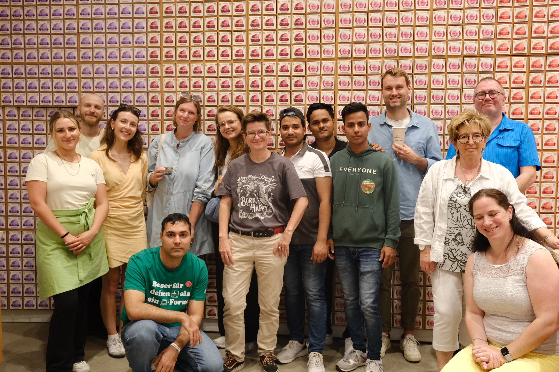 A diverse group of people smiling and posing together, with some wearing casual attire including dresses and aprons, reflecting a friendly, social gathering.