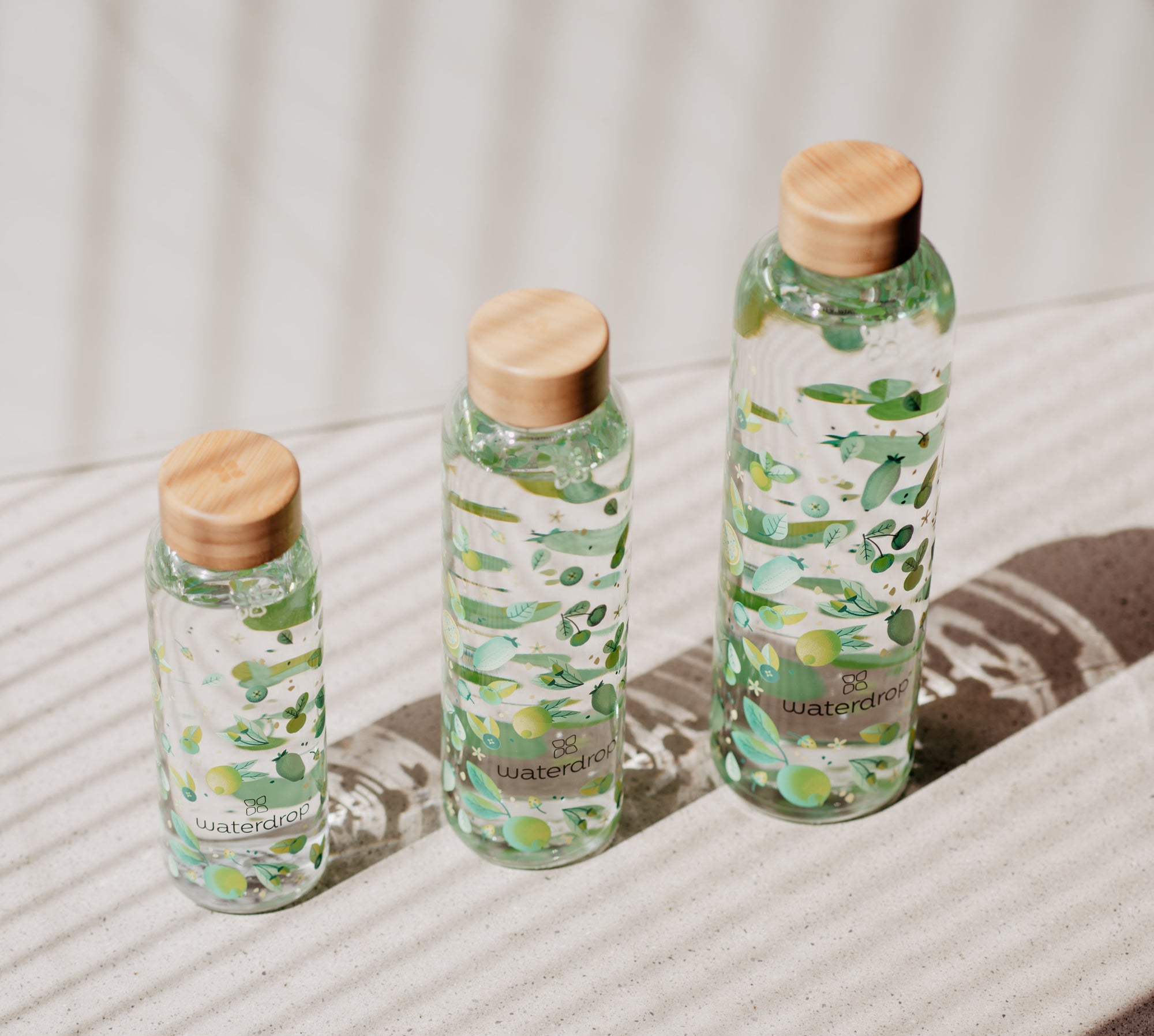 A group of waterdrop® branded bottles with water and leaves on them, alongside a glass featuring green and white designs.