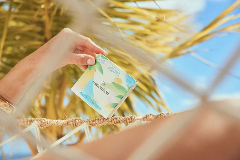 A hand holding a box on a rope against a clear sky, showcasing sustainable packaging from waterdrop® EU.