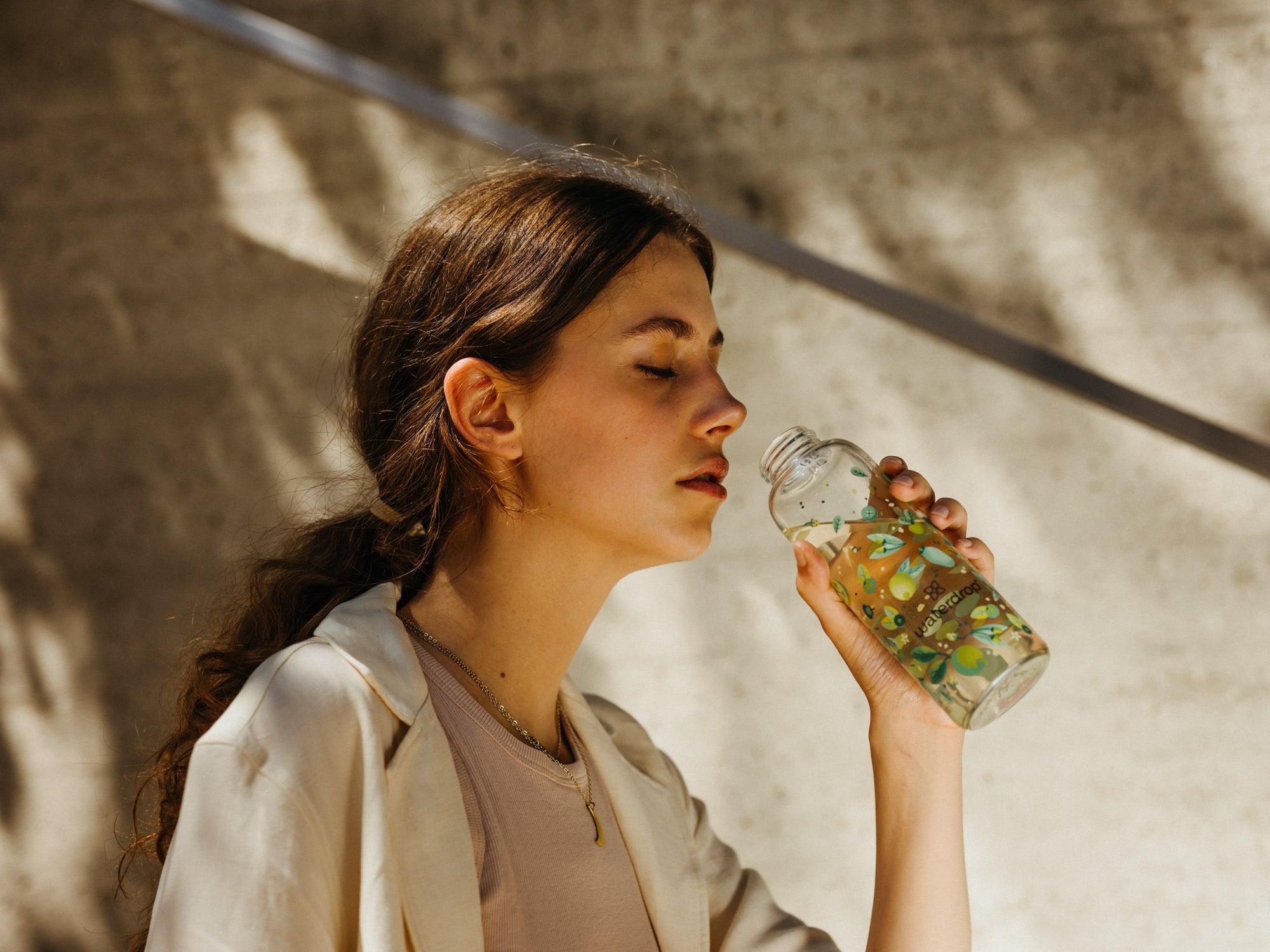 A woman drinking from a waterdrop® branded bottle, close-up.