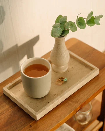 A cup of tea and a white vase with leaves on a wooden tray, reflecting a serene hydration-focused setting.
