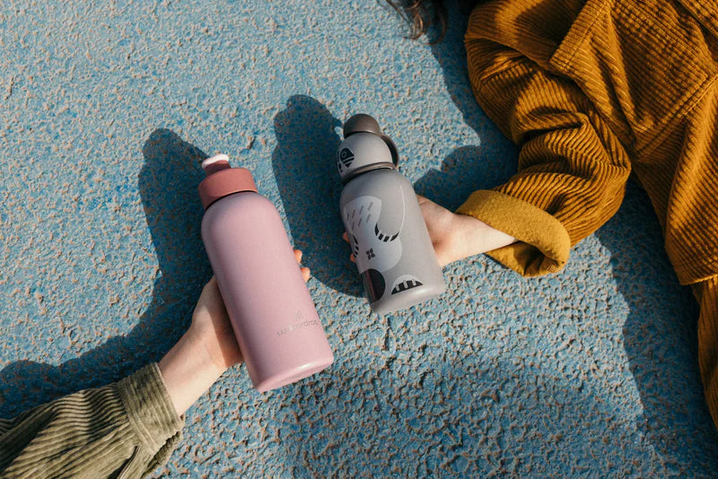 A person holding a pink waterdrop® bottle, outdoors, with visible footwear and clothing.