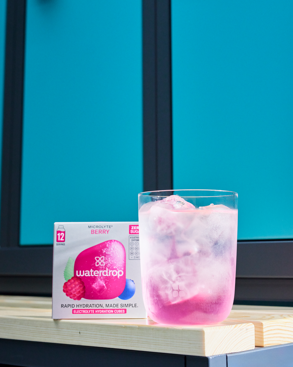 Microlyte Set: A glass of water with ice beside a 12-pack of electrolytes in four flavors—Berry, Blueberry, GRAPEFRUIT microdrink, and Melon.
