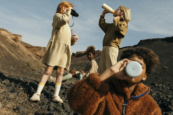Children drinking from water bottles outdoors, promoting hydration solutions by waterdrop® EU.