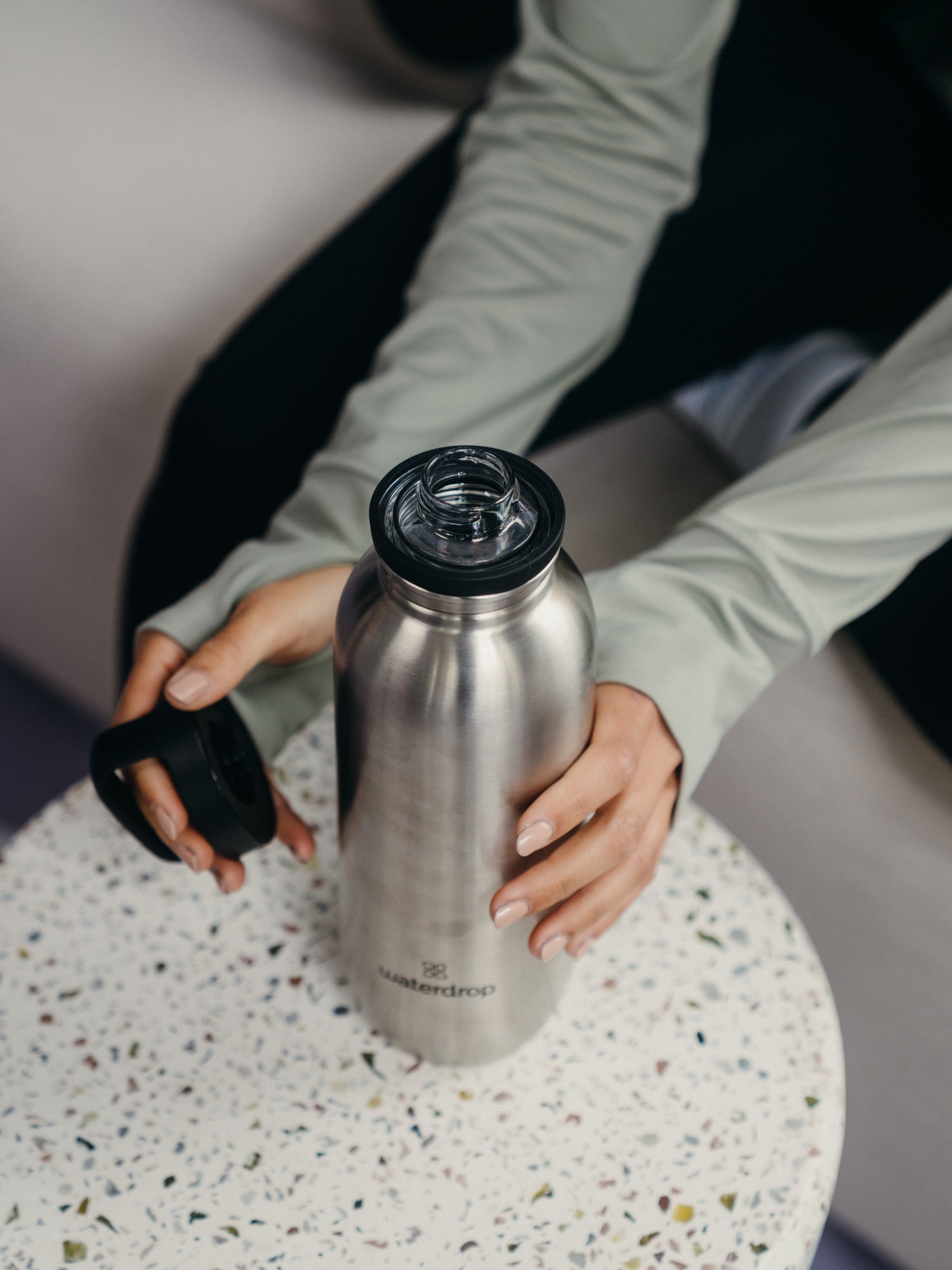 A person holding a waterdrop® branded water bottle indoors.