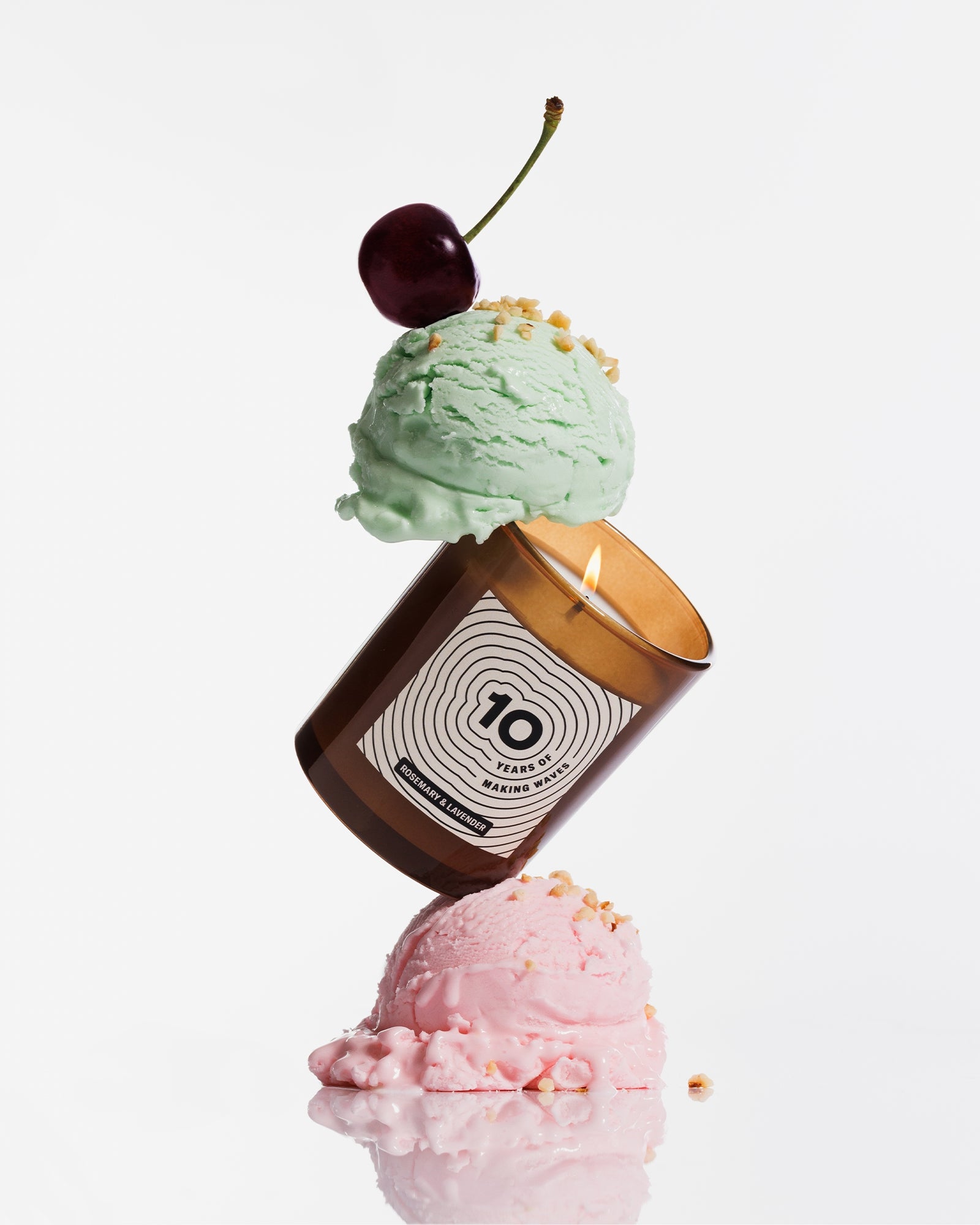 A brown candle balanced between two pastel ice cream scoops, topped with a cherry.