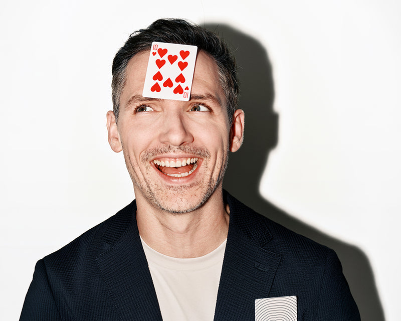 Smiling man with a playing card on his forehead against a white background.