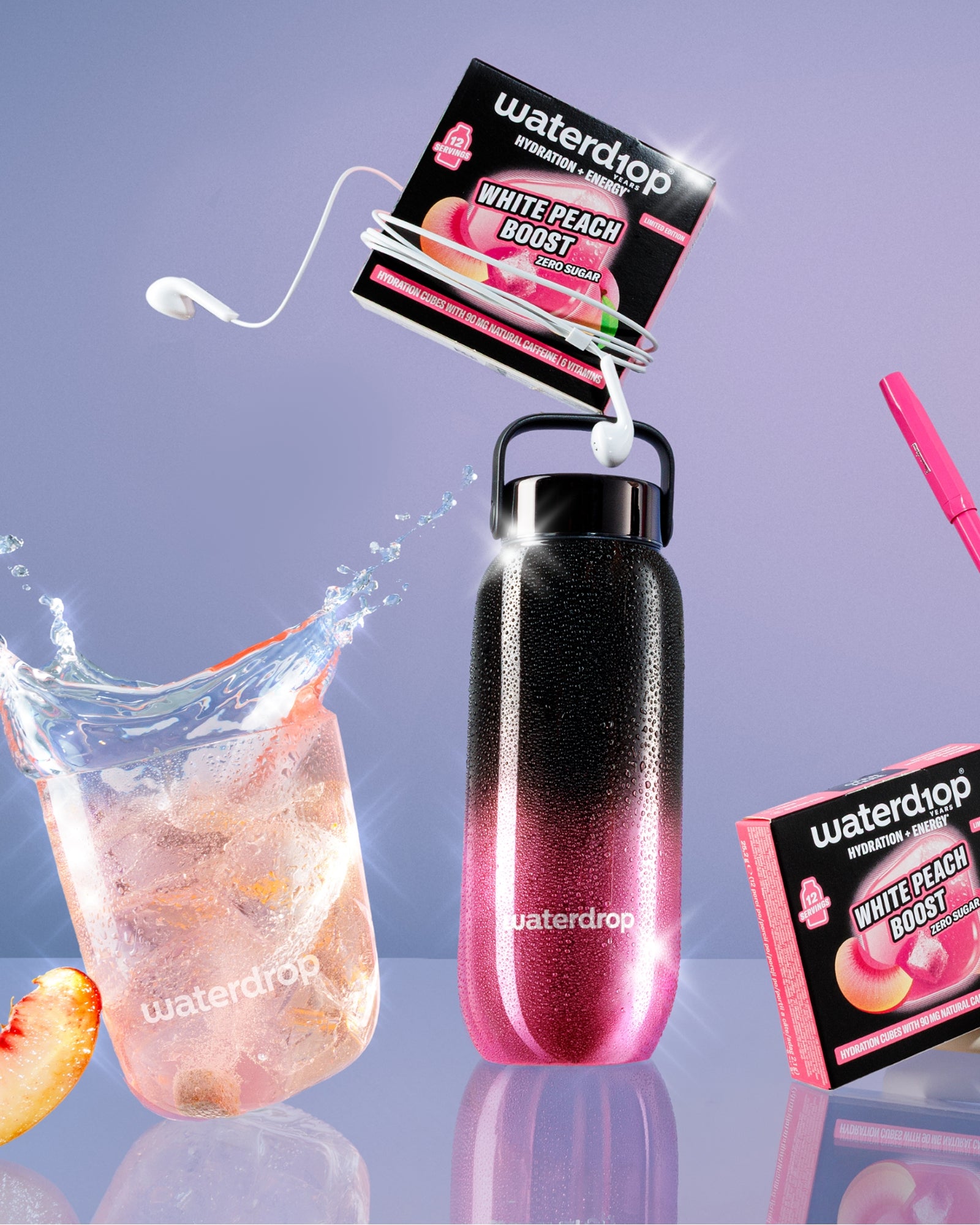 Gradient pink-to-black reusable bottle with a loop handle, connected flavor packets, a glass of ice and peach slice, and a pink straw accessory.