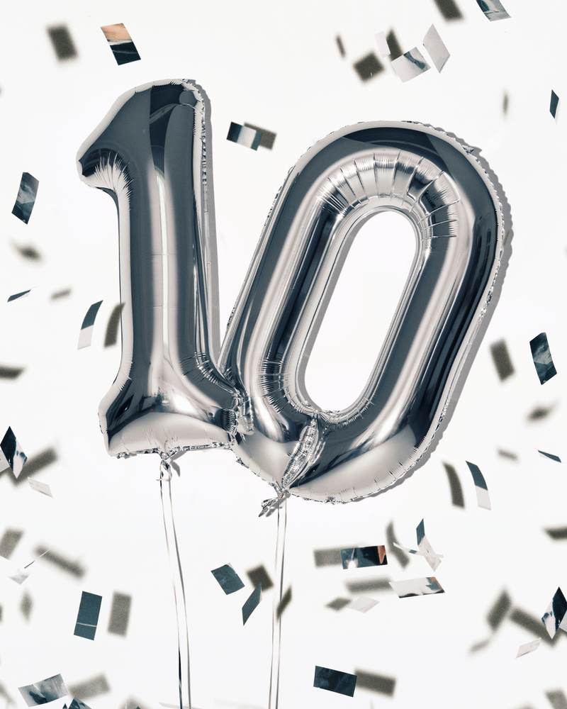 Silver foil balloons in the shape of the number 100 with strings, surrounded by confetti.