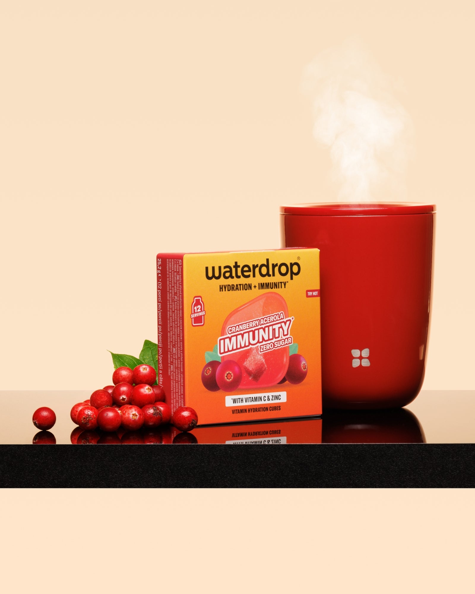 Red steaming mug next to a red-topped box and cranberries on a glossy surface.
