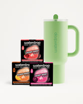 Three flavor booster boxes in orange, pink, and purple beside a light-green insulated mug with a handle.