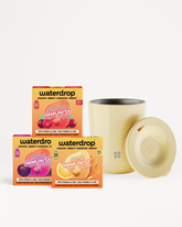 Three vitamin drink mix boxes and a beige mug with a lid on a white background.