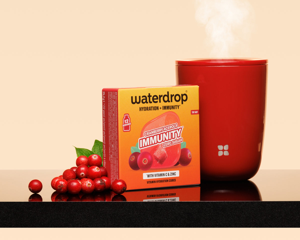 Orange box beside a steaming red mug and a cluster of red berries on a reflective surface.