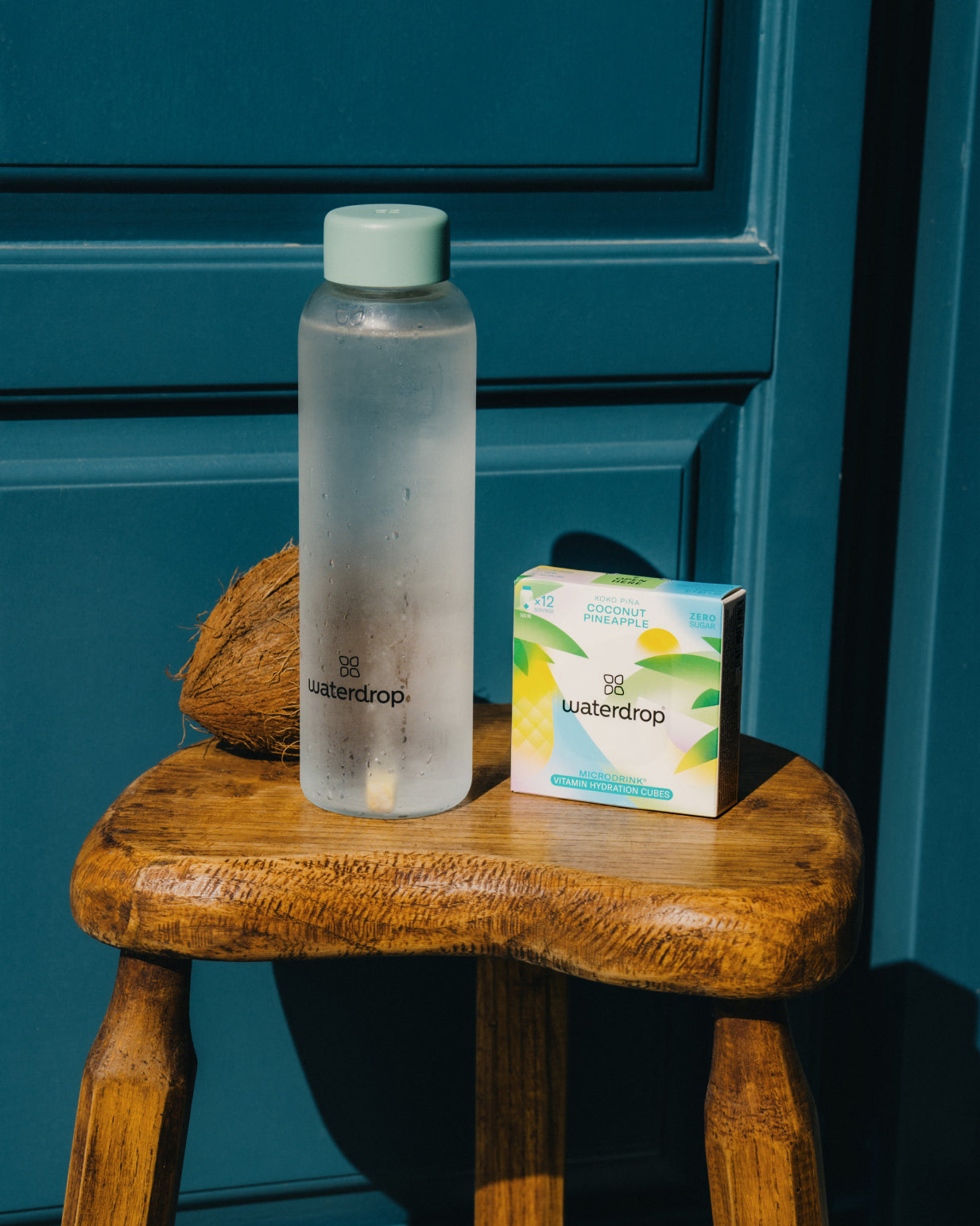 KOKO PIÑA water bottle and box on a stool, promoting tropical coconut and pineapple flavors for hydration. Limited Edition.