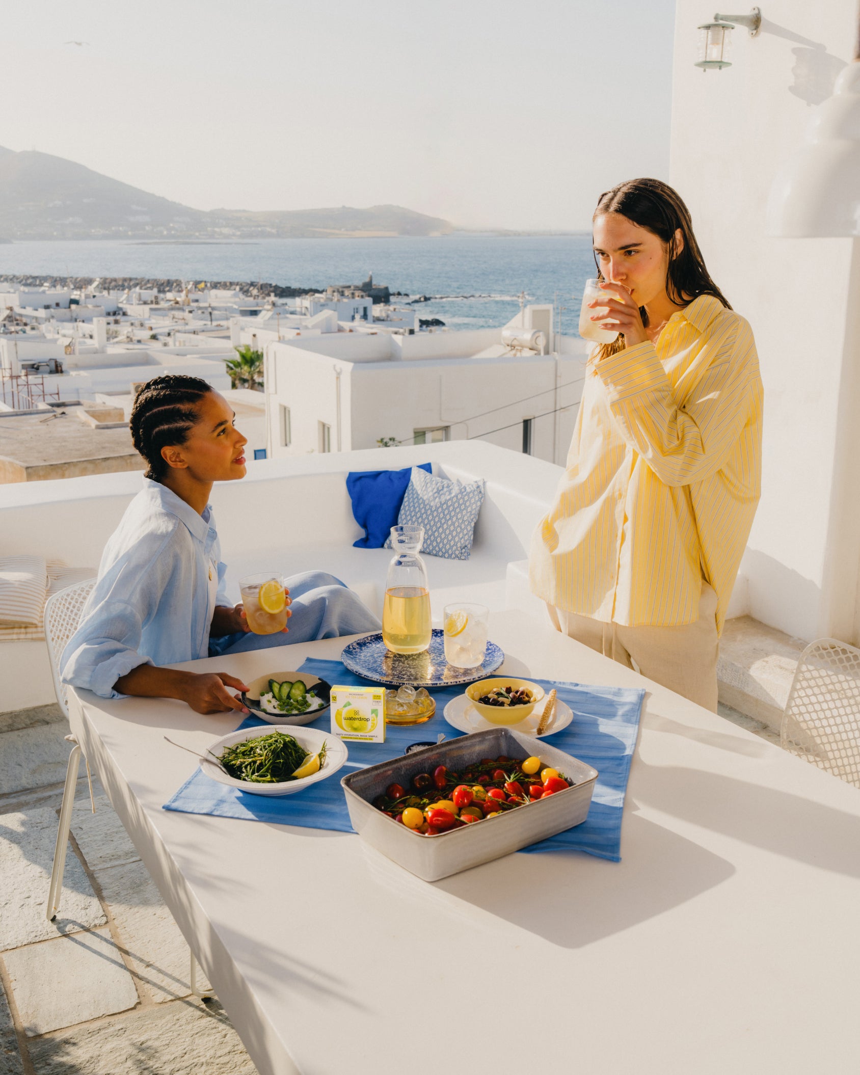 Two women enjoying ICE TEA LEMON at a table with various fresh foods and beverages.