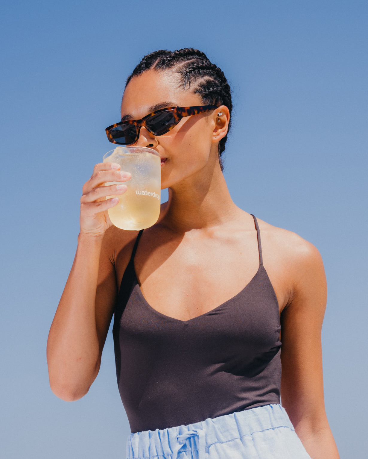 Woman drinking ICE TEA LEMON from a glass, enjoying a refreshing moment outdoors.