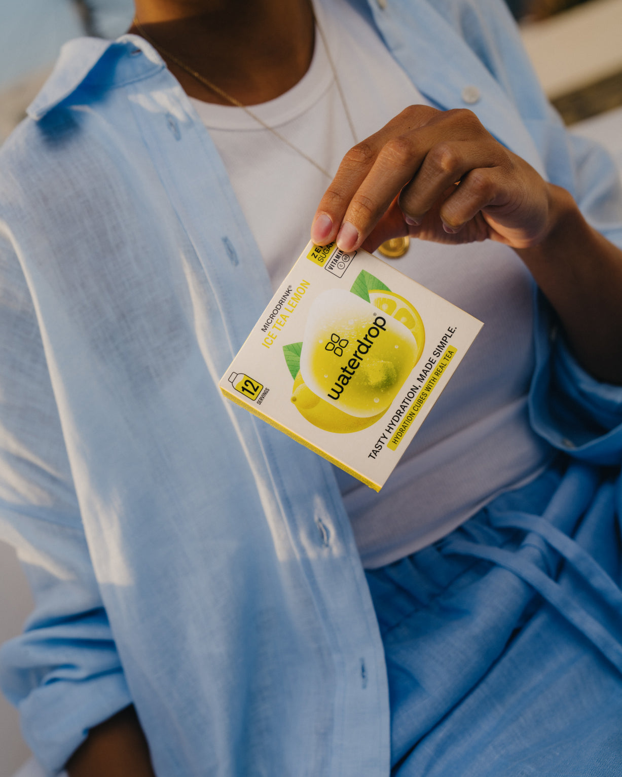 Person holding ICE TEA LEMON packet, showcasing lemon and green tea instant drink.