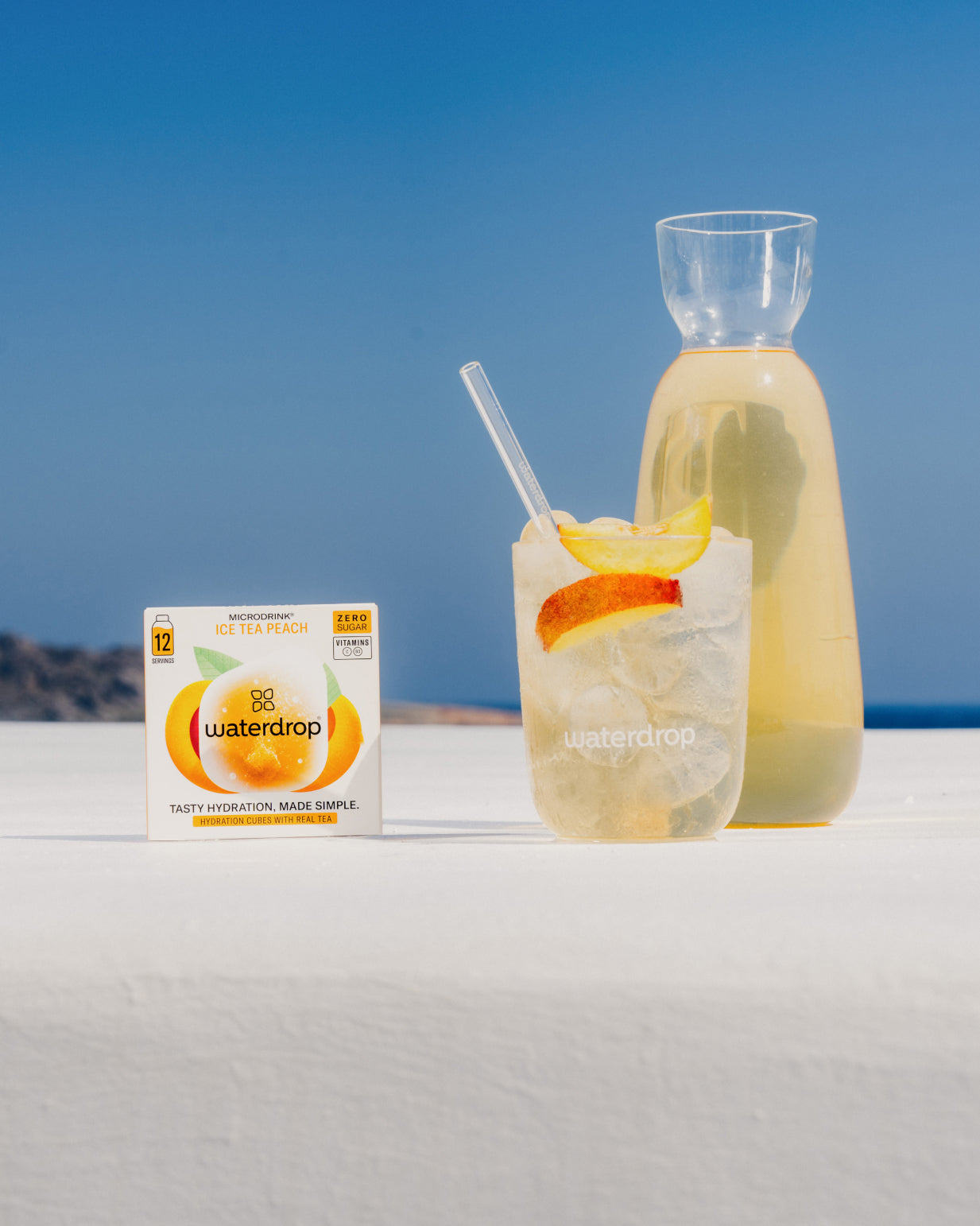 A bottle of waterdrop® ICE TEA Peach next to a glass of iced tea with a lemon slice and a branded box.