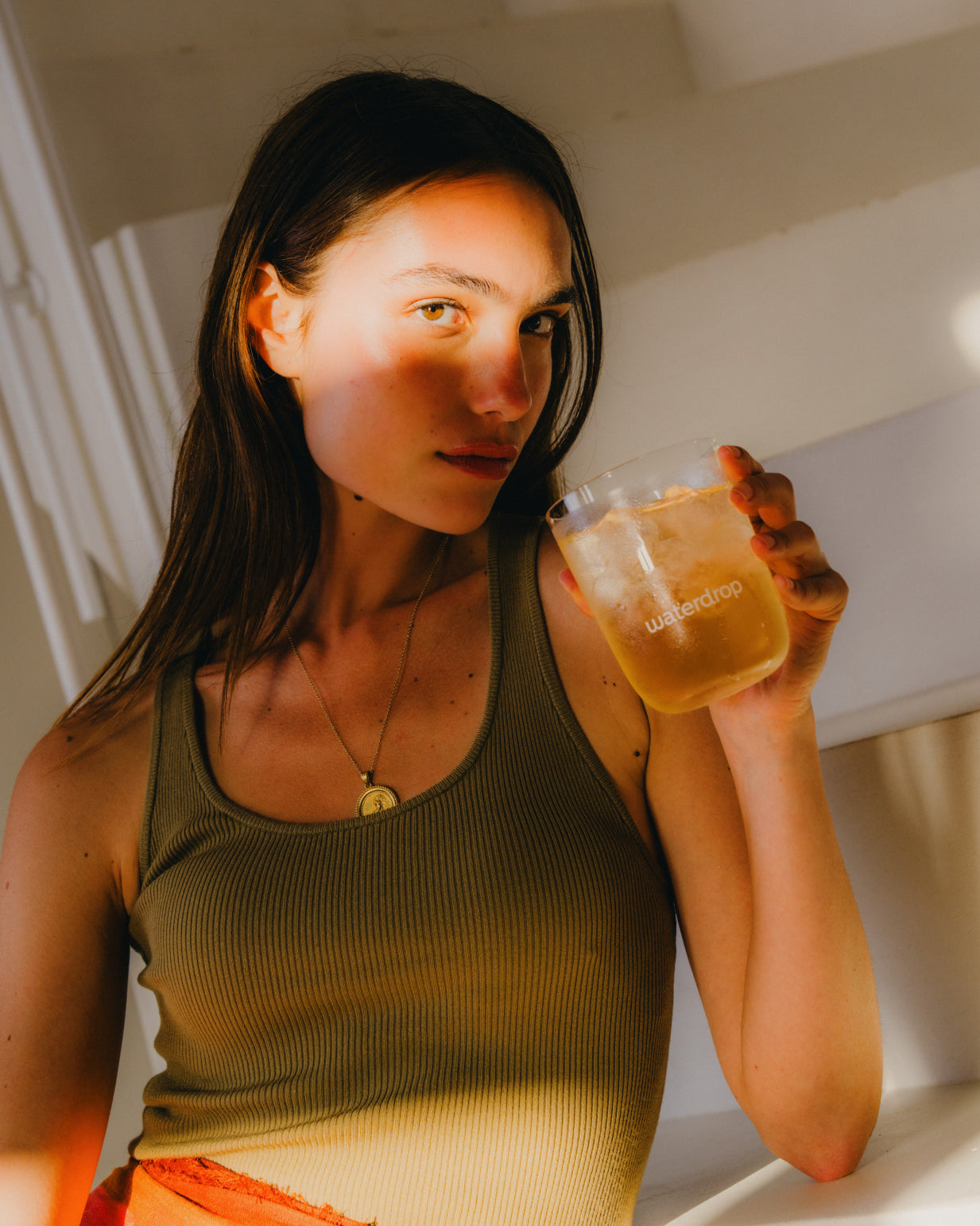 Woman holding a glass of ICE TEA Peach, showcasing a sugar-free, sweet, and fruity black tea water enhancer from waterdrop® EU.