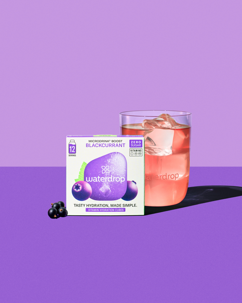 Glass of blackcurrant Microdrink and a box, highlighting the fruity, tart flavor with elderberry and açaí, from waterdrop®'s hydration solutions.
