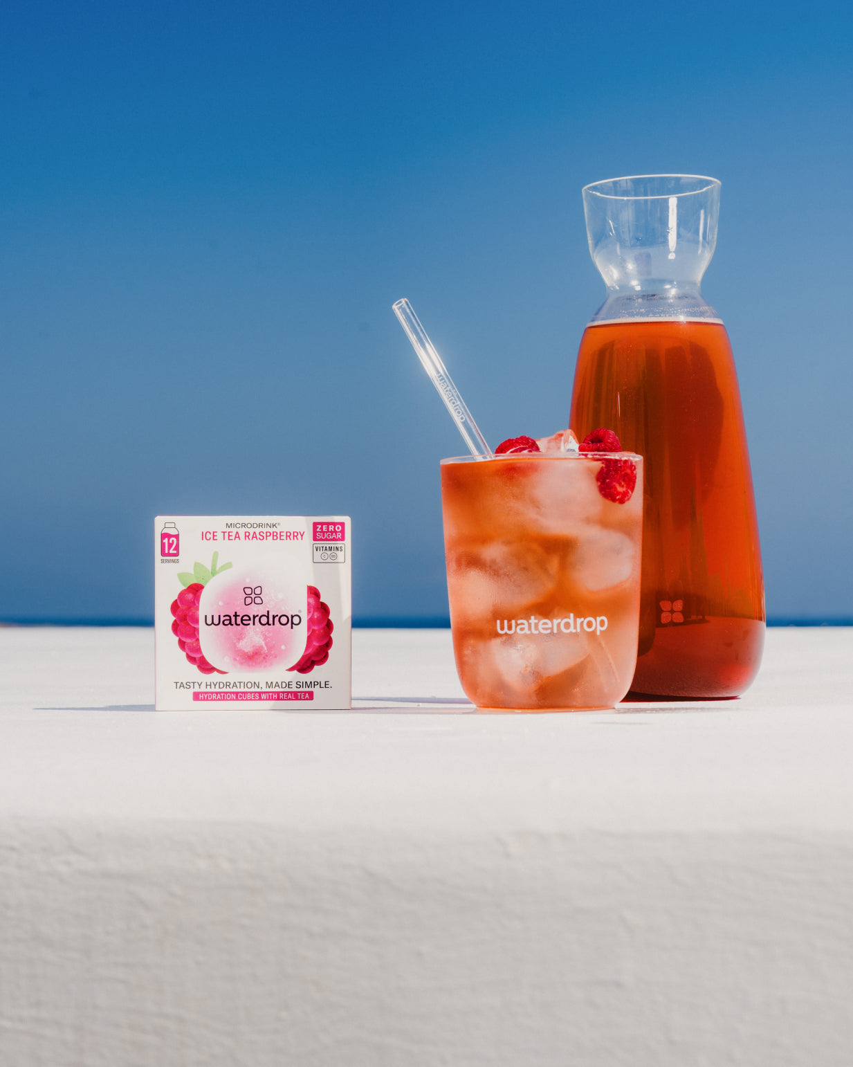 Bottle of ICE TEA RASPBERRY with straw, next to a box and glass of ice tea with raspberries.