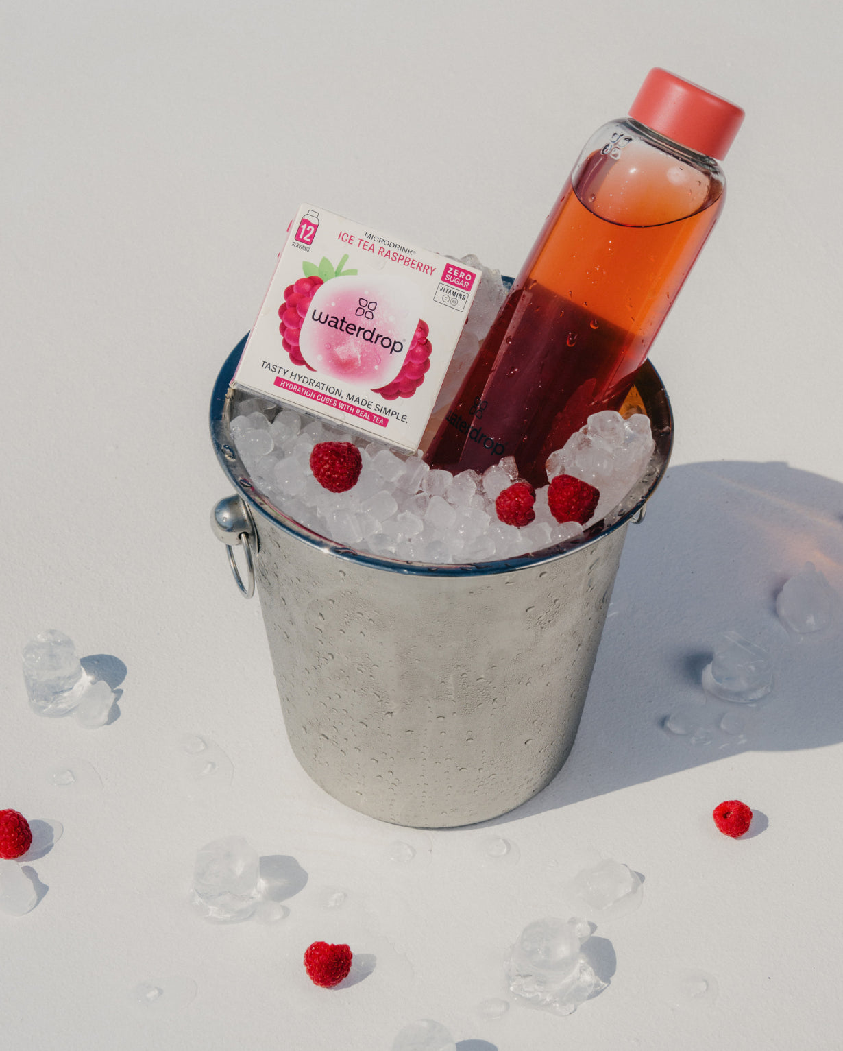 ICE TEA RASPBERRY bottle in a bucket of ice with a box of raspberries.